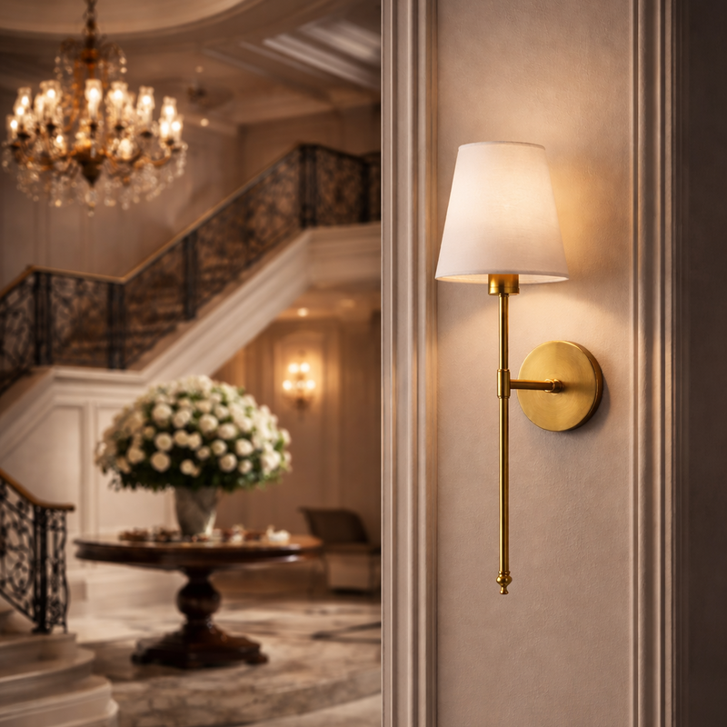 A stately Adler brass sconce with a refined linen shade anchors a classical foyer, reflecting Old Money luxury alongside a large marble staircase and chandelier.