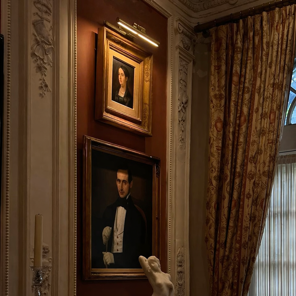 brass picture light, the Biltmore edition over stately art gallery in an upscale Victorian interior room with curtains and wainscoting panels.